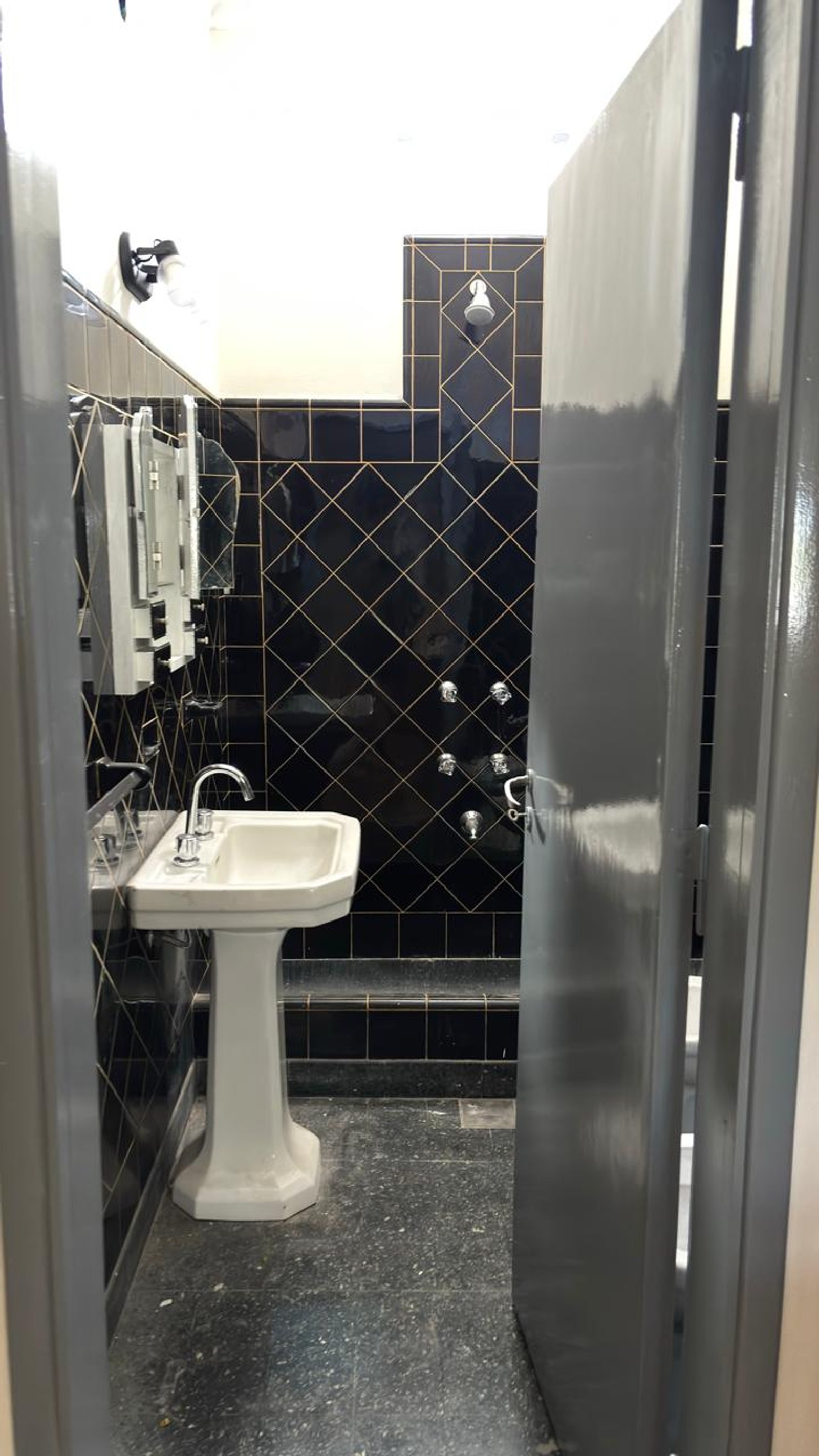 Baño comercial con azulejos negros, lavabo pedestal y ducha múltiple — proyecto REFORMA C520, por Estudio Llobet, en Melchor Romero